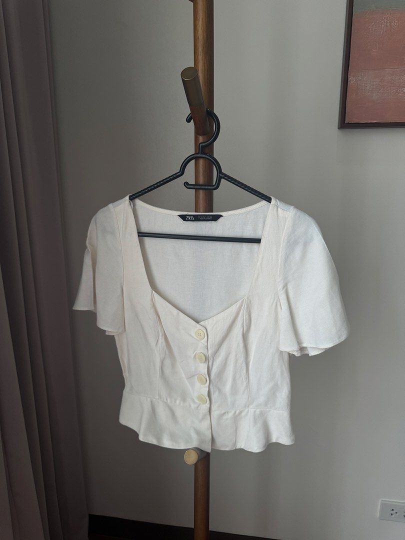 Zara White Button-Front Blouse Size S (Category: Blouses) located in Pasig City. Submitted by kutleyn (Listing ID 1465653873, Image 1). Description: - Brand: Zara - Size: S - Color: White - Design: Square neckline with button-front closure - Sleeves: Short flared sleeves - Fit: Cropped length with subtle ruffled hem - Origin: Made in Cambodia.