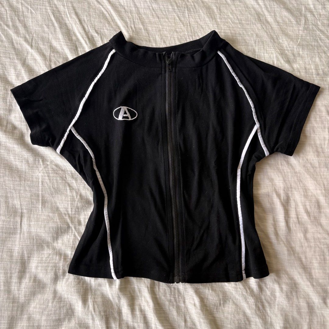 Black and white zip-up short sleeve top (Category: Blouses) located in Makati City. Submitted by jinlouise (Listing ID 1471143417, Image 2). Description: - Color: Classic black with contrasting white piping along raglan seams - Design: Full front zipper closure with a small embroidered 'A' logo patch on the right chest - Fit: Structured with a flattering tapered waistline and flared hem - Material: Comfortable ribbed cotton-blend fabric with grea