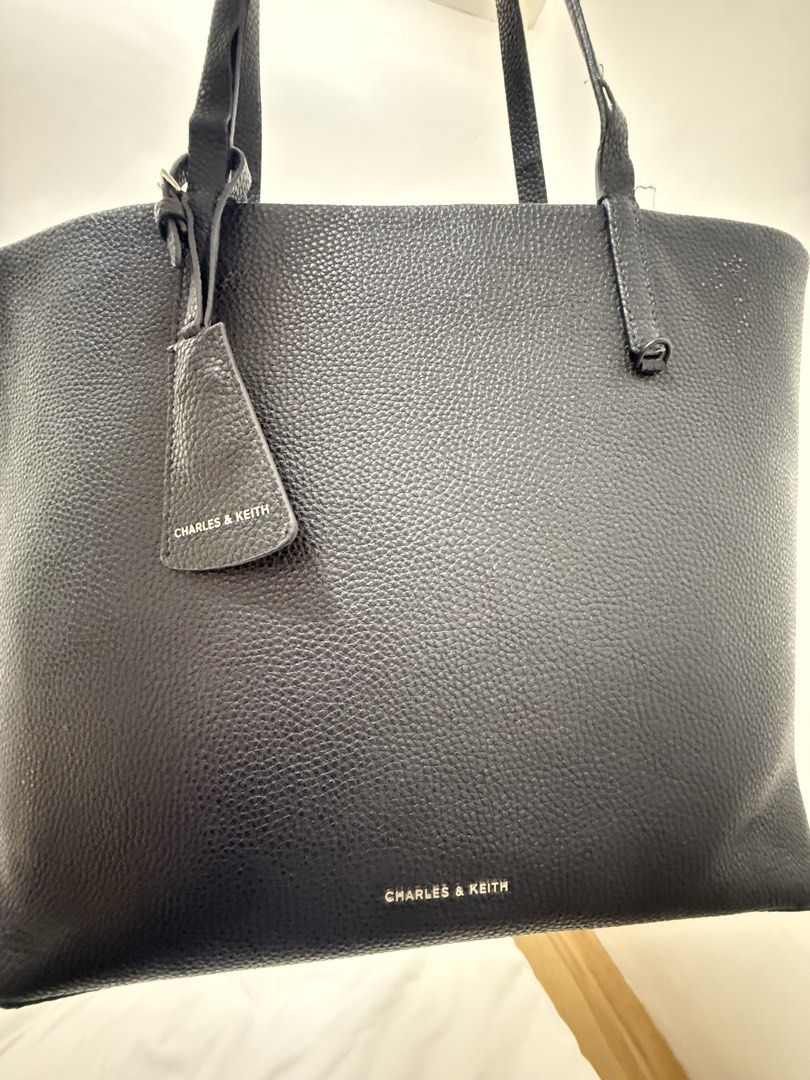 Charles & Keith Black Tote Bag 25L3W (Category: Tote Bags) located in Manila. Submitted by k.e9999 (Listing ID 1471261241, Image 1). Description: - Brand: Charles & Keith - Color: Classic Black - Material: Grainy texture faux leather with silver-tone hardware - Size: Large (Spacious everyday bag) - Features: Double shoulder straps, front branding, and dangling tag charm - Condition Note: Visible wear and peeling along the strap edges - Style Code