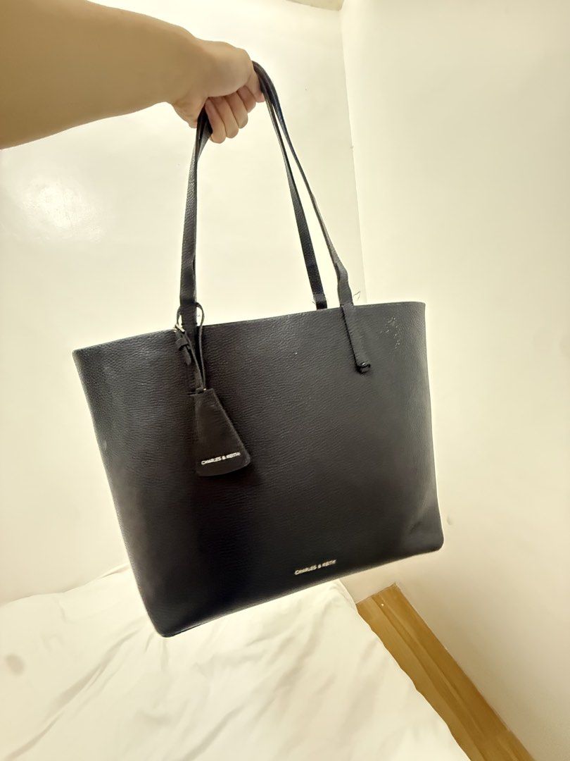 Charles & Keith Black Tote Bag 25L3W (Category: Tote Bags) located in Manila. Submitted by k.e9999 (Listing ID 1471261241, Image 2). Description: - Brand: Charles & Keith - Color: Classic Black - Material: Grainy texture faux leather with silver-tone hardware - Size: Large (Spacious everyday bag) - Features: Double shoulder straps, front branding, and dangling tag charm - Condition Note: Visible wear and peeling along the strap edges - Style Code