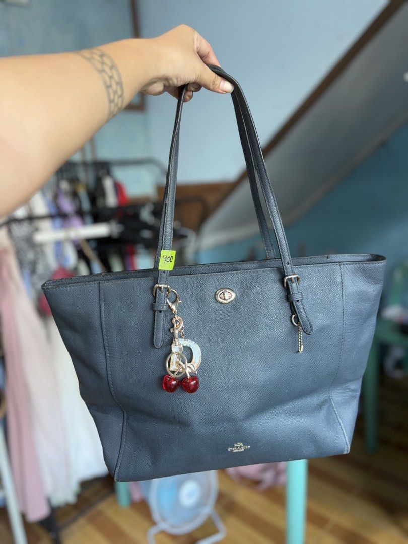 Coach Leather Tote Bag Navy Blue (Category: Luxury Bags & Wallets) located in Manila. Submitted by dorilorenr48954 (Listing ID 1471225463, Image 1). Description: - Authentic navy blue Coach tote bag in textured leather - Features dual adjustable shoulder straps and a playful double-cherry keychain - Secure zip-top closure with a spacious fabric-lined interior and Coach creed patch - Condition: Good, with minor scuffs and wear along the bottom bas