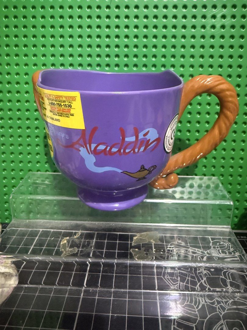 Disney Aladdin Abu Character Purple Mug (Category: Coffee & Tea Tableware) located in Victoria. Submitted by pisangpaulotoys (Listing ID 1471289055, Image 2). Description: - Disney Aladdin Abu character mug in purple - Molded Abu face on the front with his tail as the handle - Microwave and dishwasher safe - Manufactured in Thailand for Walt Disney's World on Ice - Original safety and quality testing sticker still attached - Perfect collectible f