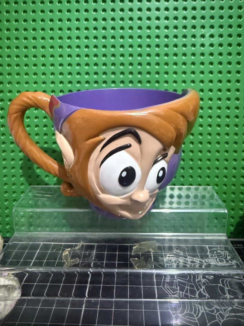 Disney Aladdin Abu Character Purple Mug (Category: Coffee & Tea Tableware) located in Victoria. Submitted by pisangpaulotoys (Listing ID 1471289055, Image 1). Description: - Disney Aladdin Abu character mug in purple - Molded Abu face on the front with his tail as the handle - Microwave and dishwasher safe - Manufactured in Thailand for Walt Disney's World on Ice - Original safety and quality testing sticker still attached - Perfect collectible f