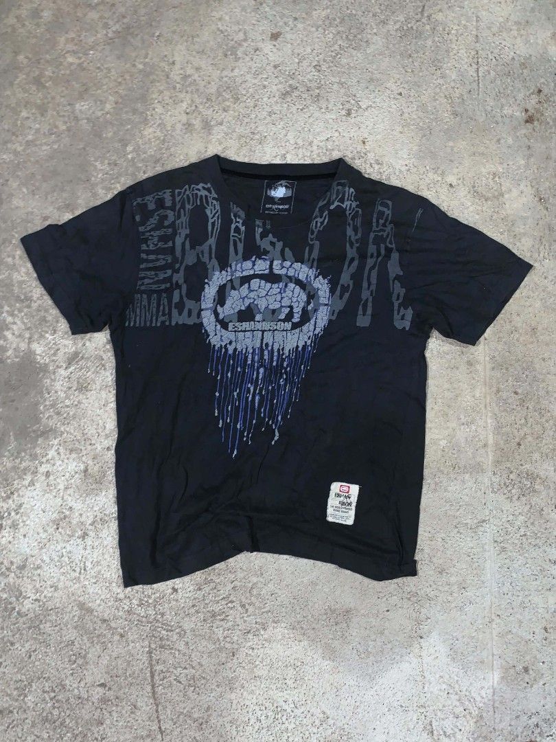 Eshannson Black Ecko (Category: Tshirts & Polo Shirts ) located in Manila. Submitted by prinxethrift (Listing ID 1471216445, Image 1). Description: - Color: Black - Size: M to L - Material: Soft cotton fabric - Design: Bold rhino graphic inside a circular emblem with dripping ink details on front and back - Detail: White tag attached near the bottom hem.