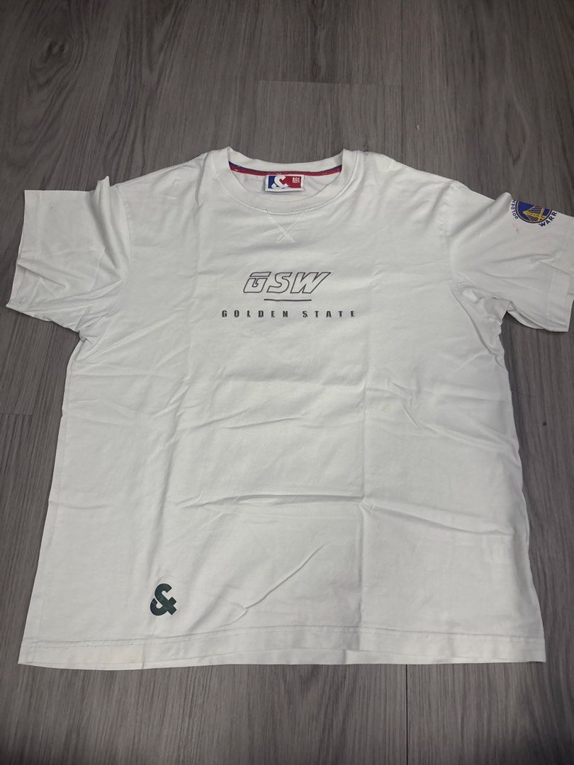 Golden State Warriors NBA White Graphic T-Shirt (Category: Tshirts & Polo Shirts ) located in Binan City. Submitted by rre1yes (Listing ID 1471237147, Image 1). Description: - Authentic Golden State Warriors white t-shirt - Front features GSW text logo and official NBA collar tag - Sleeve is accented with a team patch - Back showcases a large, colorful vertical Warriors graphic - Designed with a comfortable ribbed crew neck - Perfect for fans and