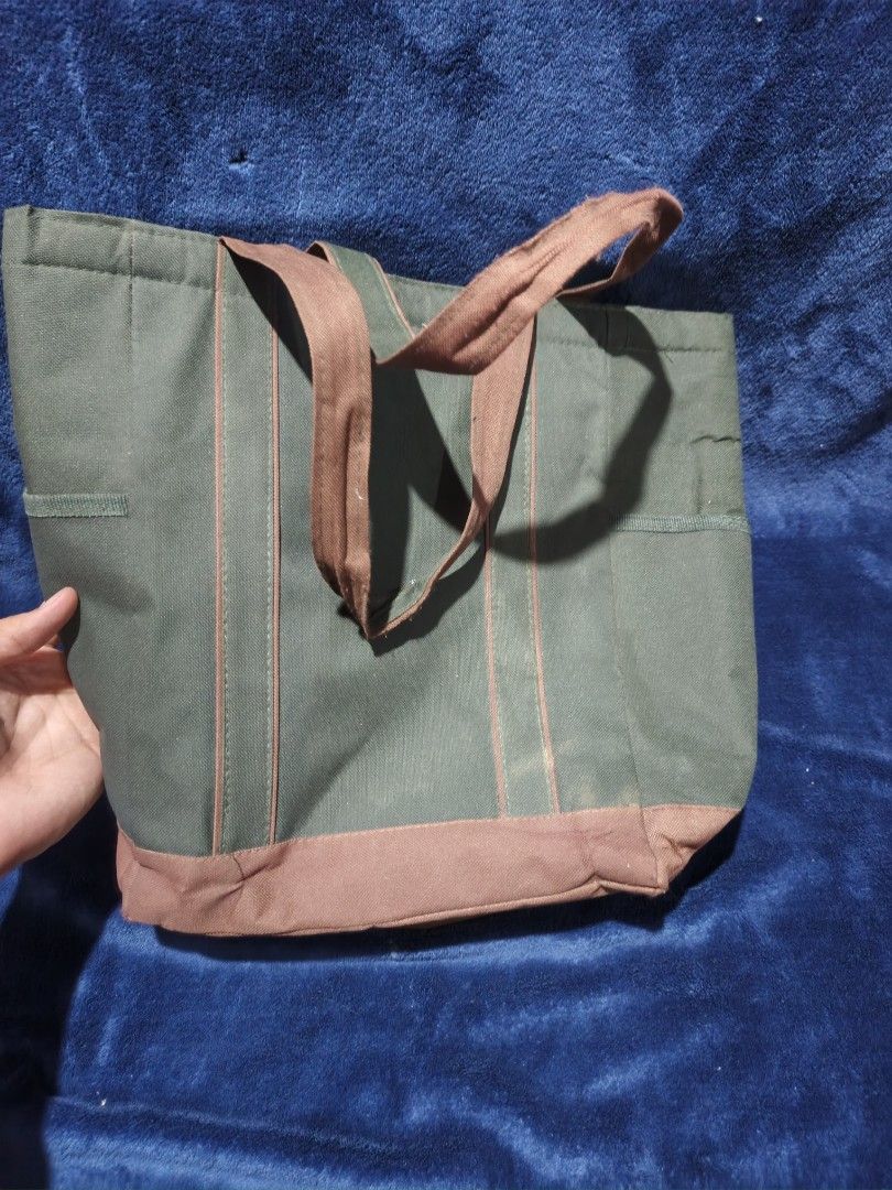 Green and Brown Canvas Tote Bag with Pockets (Category: Tote Bags) located in Manila. Submitted by kirstentoyshub (Listing ID 1471251721, Image 2). Description: - Color: Green canvas with brown base and straps - Storage: Front slip pocket, side pockets on both ends, and a roomy cream-lined interior with a dark compartment floor - Design: Durable and sturdy construction - Usage: Ideal everyday carryall with spacious capacity for all your daily ess