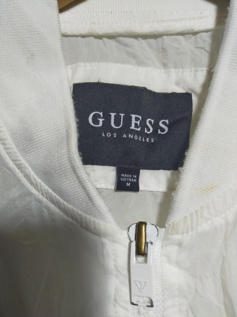 Guess Los Angeles White Bomber Jacket Size M (Category: Coats, Jackets and Outerwear) located in Valencia. Submitted by cabisaythriftshop (Listing ID 1471221935, Image 3). Description: - Brand: Guess Los Angeles - Item: Nylon Bomber Jacket - Color: White - Size: Medium - Features: Zip-up front, matching white zipper pulls, ribbed cuffs/collar/hem, triangular logo patch on chest, utility zipper pocket on left sleeve - Material: Lightweight, ideal 