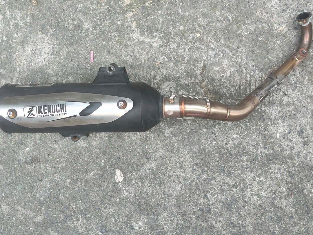 Kenochi Motorcycle Exhaust Pipe System (Category: Mufflers, Exhaust Parts & Accessories) located in Quezon City. Submitted by jcccccccccccccc (Listing ID 1471139904, Image 1). Description: - Brand: Kenochi exhaust pipe setup - Compatibility: Suitable for scooters and underbone motorcycles - Inclusions: Black muffler canister with silver heat shield, header pipes, spring clamps, and mounting points - Condition: Noticeable heavy scratches and wear 