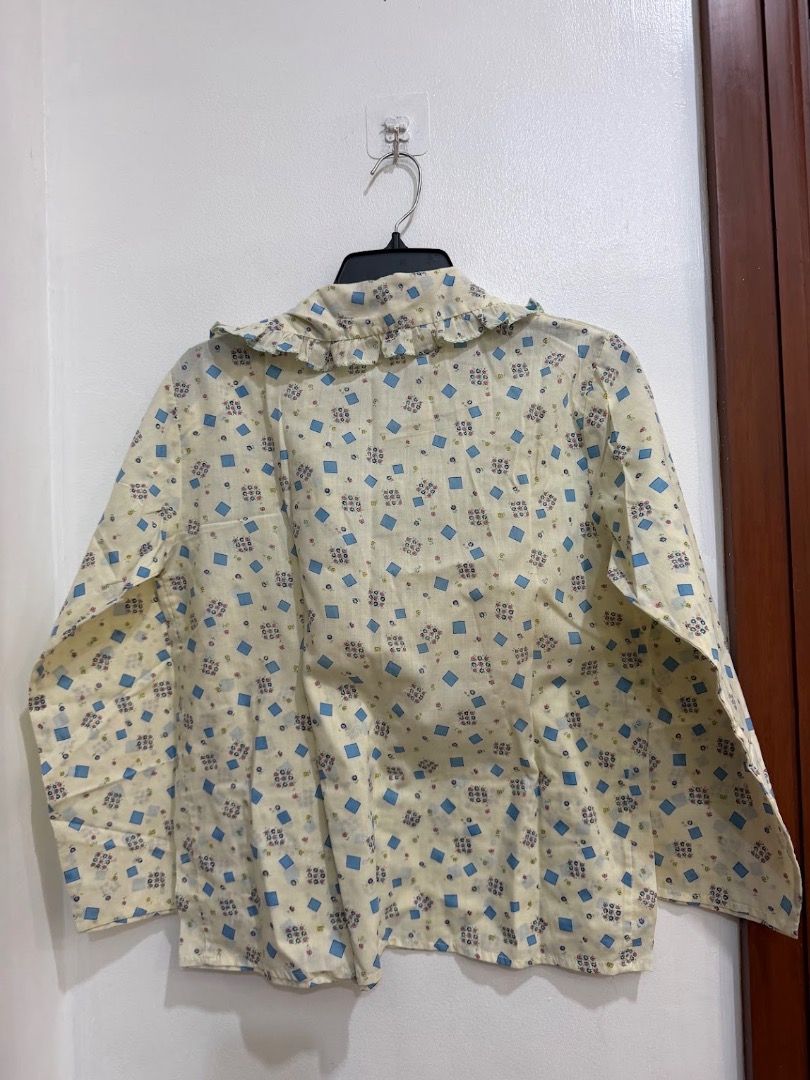Korean Yellow Blue Pattern Long Sleeve Button Down Polo Blouse Ruffle Collar (Category: Blouses) located in Quezon City. Submitted by decluttering_alot (Listing ID 1471183983, Image 2). Description: - Color & Pattern: Light yellow with all-over blue geometric and floral prints - Design: Long sleeves, button-up front, ruffled collar neckline, and structured shoulders - Fabric: Lightweight, comfortable, and easy to style with skirts or pants - Cond