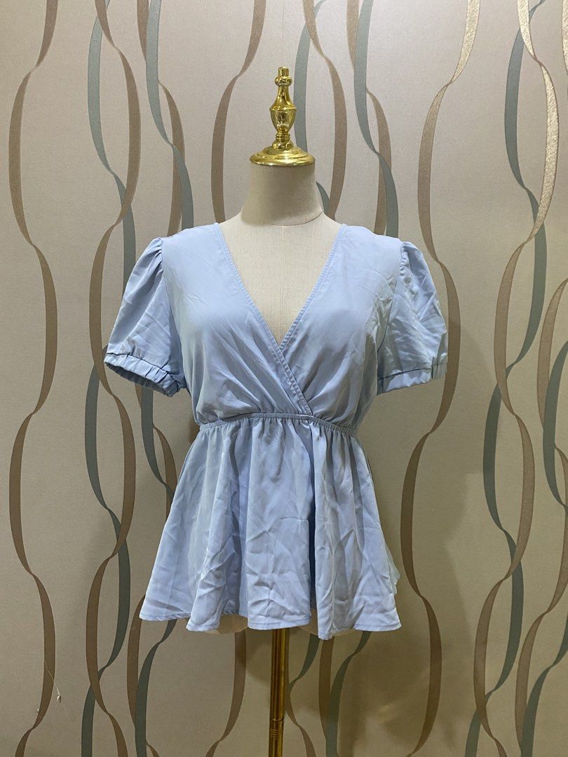 Light blue wrap top with puff sleeves (Category: Blouses) located in Marikina City. Submitted by lovegoeson (Listing ID 1471125910, Image 2). Description: - Color: Light blue - Style: Wrap blouse with V-neckline and crossover front - Sleeves: Short puff sleeves - Fit: Elasticated waist with a flattering peplum silhouette - Material: Soft and flowy fabric - Versatile: Easy to match with jeans or skirts for casual days.