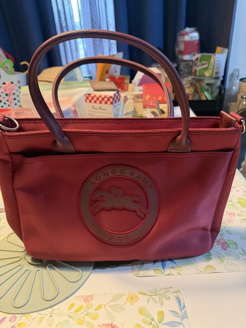 Longchamp Red Tote Bag (Category: Luxury Bags & Wallets) located in Manila. Submitted by fitandshop (Listing ID 1471263127, Image 1). Description: - Authenticity not guarantee red Longchamp tote bag - Features bold front circular Longchamp 1948 logo patch - Structured fabric body with comfortable double top handles - Open top design with a handy front slip pocket - Spacious interior with great depth for daily essentials - Clean shape, ideal for e
