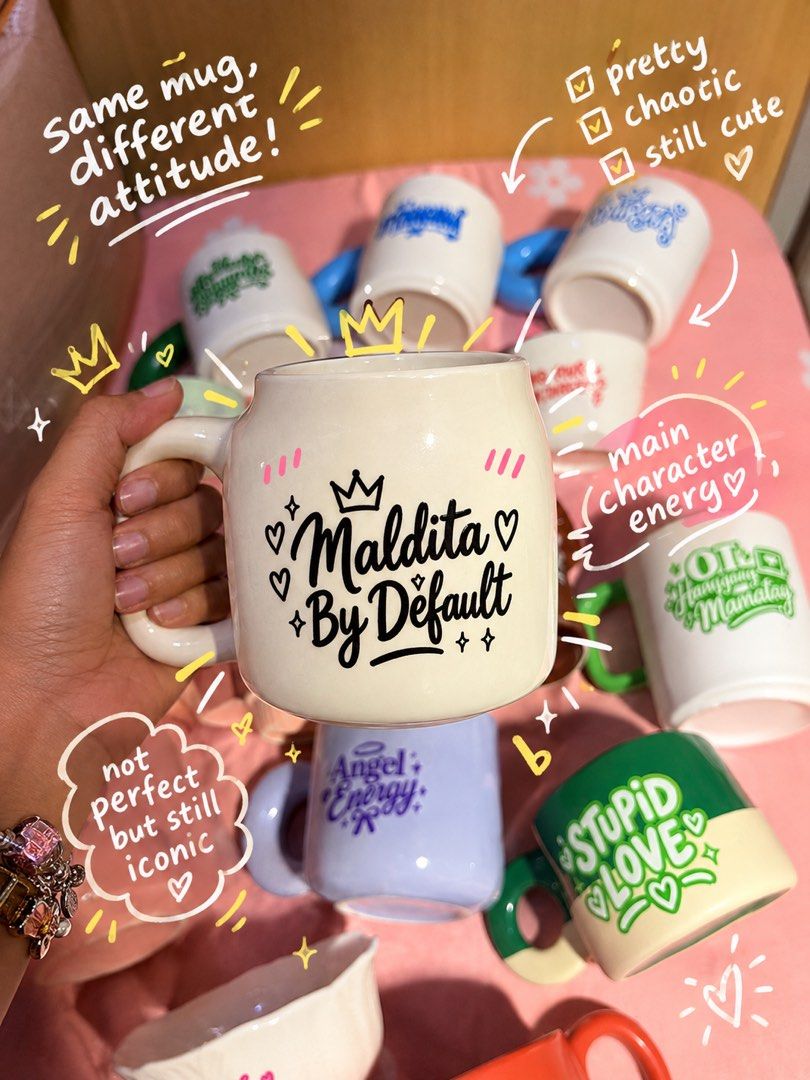 Maldita By Default Ceramic Mug (Category: Coffee & Tea Tableware) located in Manila. Submitted by kniccknacks (Listing ID 1471182996, Image 1). Description: - Design: White ceramic mug featuring 'Maldita By Default' in black script with crown, star, and heart graphics - Details: Chic pink stripes near the rim and a comfortable chunky handle - Vibe: Quirky, sassy attitude drinkware—ideal for your morning coffee or as a gift - Condition: Brand new 