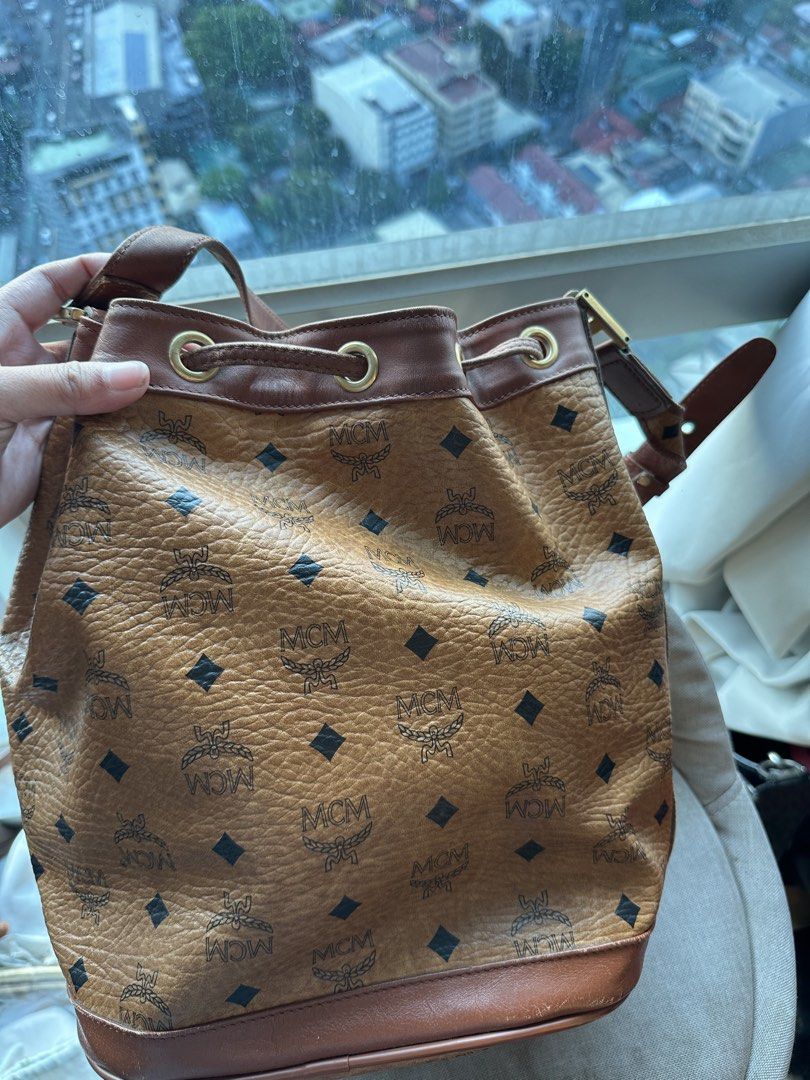 MCM Visetos Monogram Leather Bucket Bag (Category: Luxury Bags & Wallets) located in Imus. Submitted by ann__xoxo (Listing ID 1471165439, Image 3). Description: - Authentic MCM bucket bag in classic brown monogram coated canvas - Dark brown leather trim and gold-tone hardware - Secure drawstring closure with an adjustable shoulder strap - MCM monogram fabric interior lining with a convenient zippered pocket - Features the iconic serial number pla