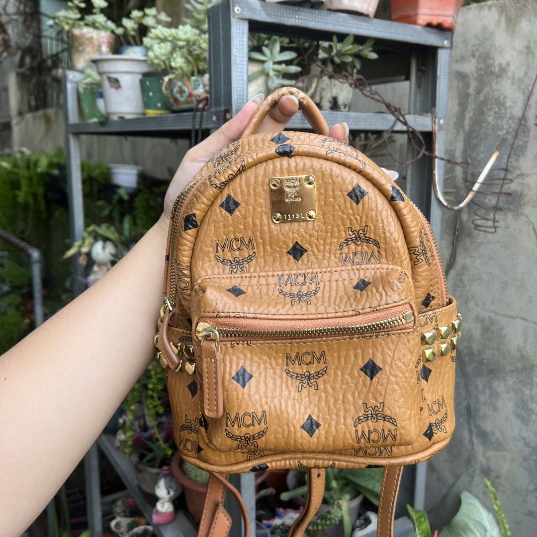 MCM Visetos Monogram Studded Mini Backpack Cognac (Category: Luxury Bags & Wallets) located in Davao. Submitted by ange030405 (Listing ID 1471165862, Image 1). Description: Cognac Visetos monogram coated canvas mini backpack by MCM. Iconic all-over print with black diamonds and laurel motif. Gold-tone hardware, metal logo plaque reading 1113L, and pyramid studs on both side pockets. Front zippered compartment, top handle, and adjustable convertib