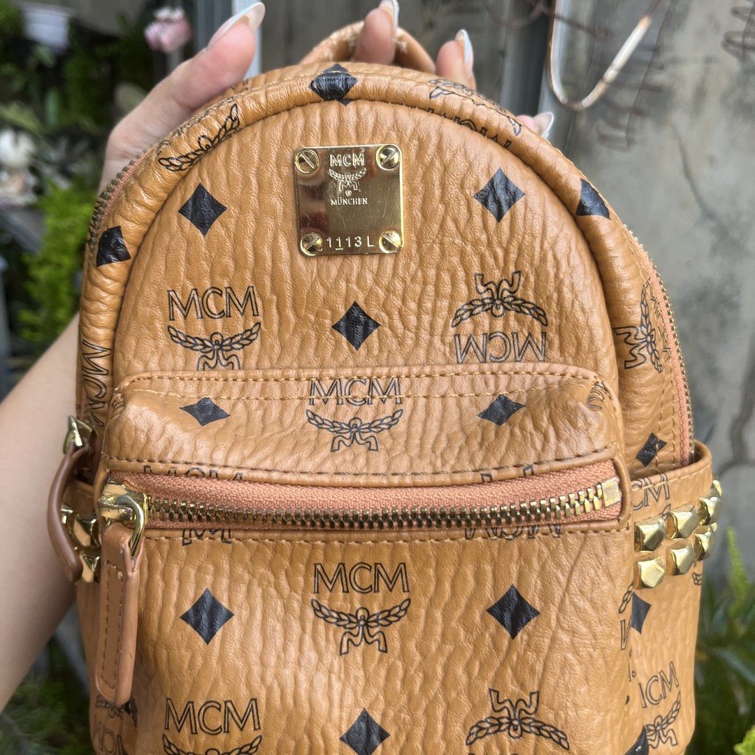 MCM Visetos Monogram Studded Mini Backpack Cognac (Category: Luxury Bags & Wallets) located in Davao. Submitted by ange030405 (Listing ID 1471165862, Image 2). Description: Cognac Visetos monogram coated canvas mini backpack by MCM. Iconic all-over print with black diamonds and laurel motif. Gold-tone hardware, metal logo plaque reading 1113L, and pyramid studs on both side pockets. Front zippered compartment, top handle, and adjustable convertib