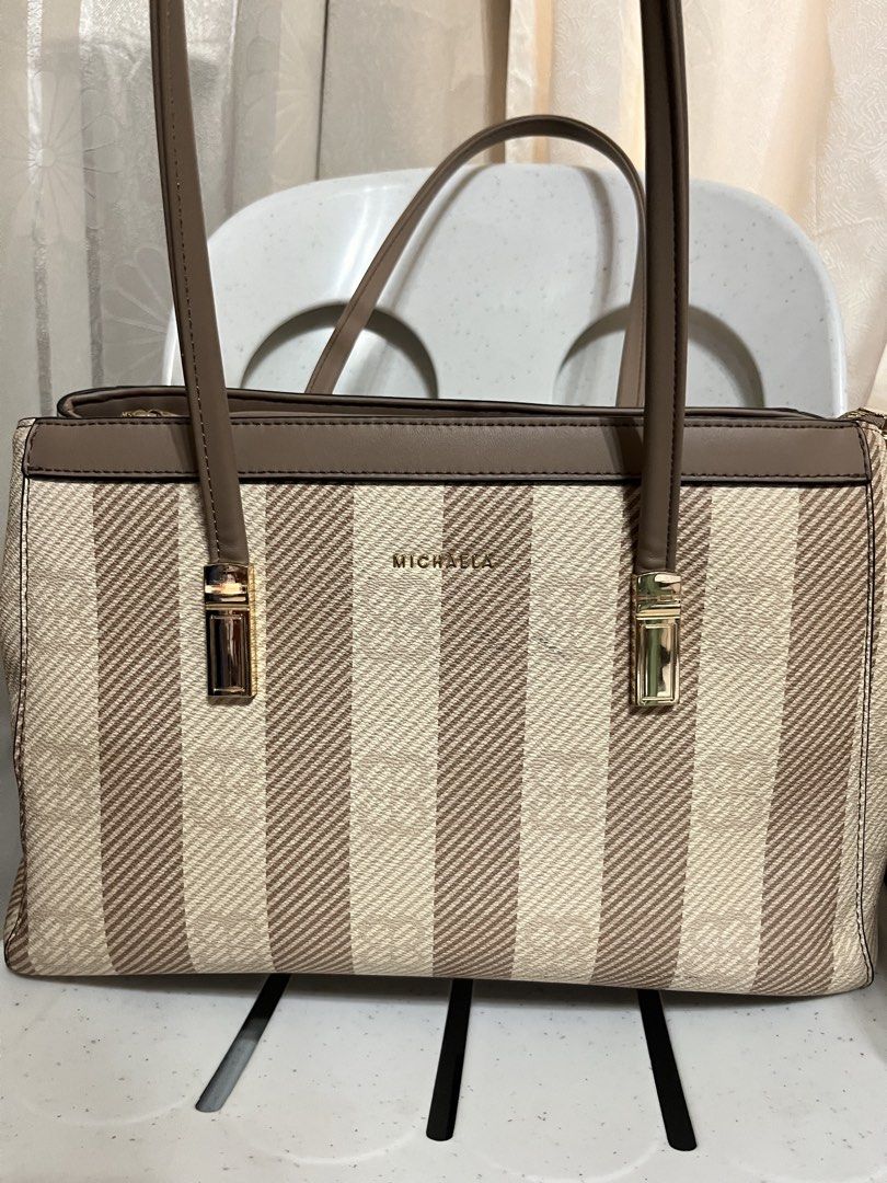 MICHAELA Striped Tote Bag Brown Beige (Category: Tote Bags) located in Koronadal. Submitted by hiiiii.hello (Listing ID 1471130923, Image 1). Description: - Color: Classic brown and beige stripes - Hardware: Elegant gold-toned details - Straps: Sturdy and comfortable for shoulder wear - Interior: Multiple zippered compartments for easy organization - Lining: Clean fabric with stylish logo prints.