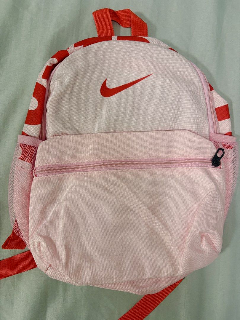 Nike Pink and Red Mini Backpack (Category: Backpacks) located in Manila. Submitted by jrpororo (Listing ID 1471233620, Image 1). Description: - Authentic Nike mini backpack in a vibrant pink and red colorway - Features a large Nike Swoosh logo on the front zipper pocket - Convenient mesh side pockets for water bottles - Comfortable black breathable mesh padding on the back panel - Adjustable red straps with durable black plastic buckles - Include