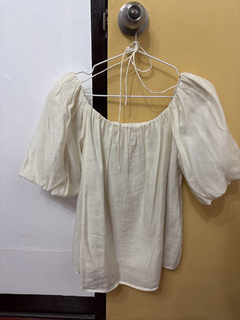 Off shoulder white puff sleeve blouse (Category: Blouses) located in Cavite. Submitted by luisascloset_ (Listing ID 1471216190, Image 3). Description: - Color: Off-white - Design: Off-shoulder with puffy half-sleeves - Details: Gathered neckline with adjustable front string ties - Fabric: Lightweight and flowy - Fit: Free size - Styling: Easy to pair with skirts or denim.