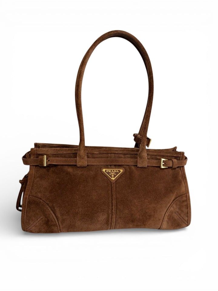 Prada Brown Suede Shoulder Bag (Category: Luxury Bags & Wallets) located in Pagadian. Submitted by therencethewarriormom (Listing ID 1471153928, Image 2). Description: Prada brown suede shoulder bag with dual top handles. Structured shape featuring gold-tone hardware, buckle belt accents along the perimeter, and the iconic triangular logo plaque on the front. Side profile shows a drawstring closure mechanism. Clean suede finish throughout with re