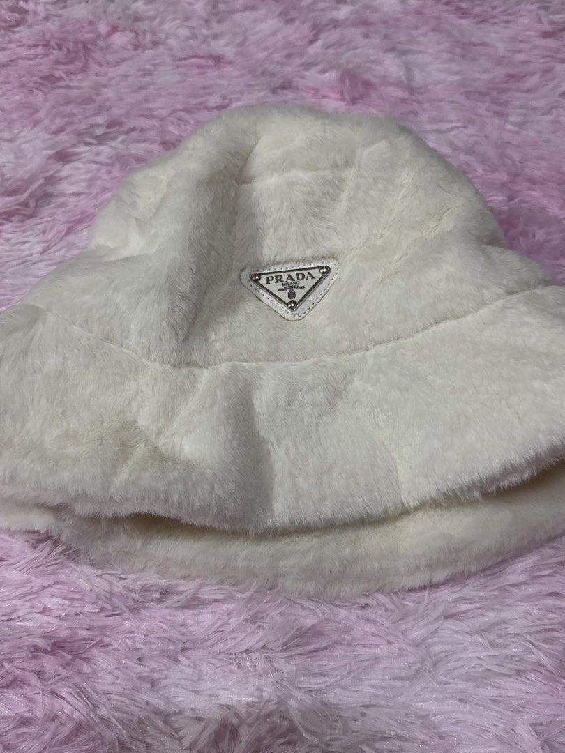 Prada White Faux Fur Bucket Hat (Category: Hats & Beanies) located in Bacoor. Submitted by micsr (Listing ID 1471223696, Image 1). Description: - Brand: Prada - Item: Fluffy faux fur bucket hat - Color: White - Features: Iconic triangular metal logo on front, interior Prada Milano fabric label - Condition: Clean overall condition, ready to wear - Style: Cozy, warm, and stylish winter accessory.