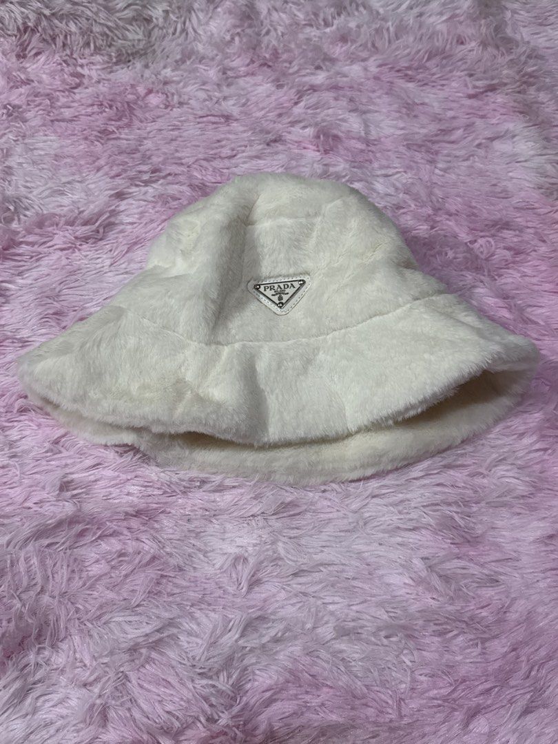 Prada White Faux Fur Bucket Hat (Category: Hats & Beanies) located in Bacoor. Submitted by micsr (Listing ID 1471223696, Image 2). Description: - Brand: Prada - Item: Fluffy faux fur bucket hat - Color: White - Features: Iconic triangular metal logo on front, interior Prada Milano fabric label - Condition: Clean overall condition, ready to wear - Style: Cozy, warm, and stylish winter accessory.
