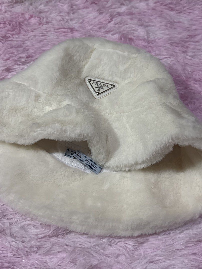 Prada White Faux Fur Bucket Hat (Category: Hats & Beanies) located in Bacoor. Submitted by micsr (Listing ID 1471223696, Image 3). Description: - Brand: Prada - Item: Fluffy faux fur bucket hat - Color: White - Features: Iconic triangular metal logo on front, interior Prada Milano fabric label - Condition: Clean overall condition, ready to wear - Style: Cozy, warm, and stylish winter accessory.