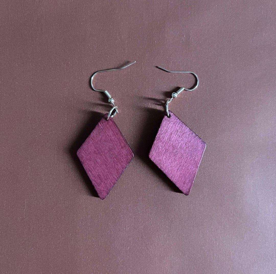Purple diamond shaped wooden dangle earrings (Category: Earrings) located in Kananga. Submitted by aurylien.clo (Listing ID 1471130994, Image 1). Description: - Handmade wooden rhombus earrings - Painted in a rich purple shade with natural wood grain texture - Silver-toned fishhook ear wires with secure jump rings - Lightweight and comfortable for everyday use - Clean edges and intact hardware.