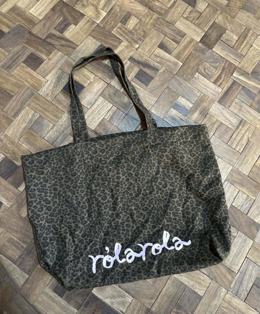 Rolarola Tote Bag (Category: Tote Bags) located in Manila. Submitted by stephsalamat (Listing ID 1471195330, Image 1). Description: - Brand: Rolarola - Material: Durable canvas in a stylish dark leopard print - Design: White handwritten-style logo near the bottom - Closure: Top snap button - Storage: Convenient zippered inner pocket - Utility: Long shoulder straps for easy carrying, ideal for daily use, school, or errands.