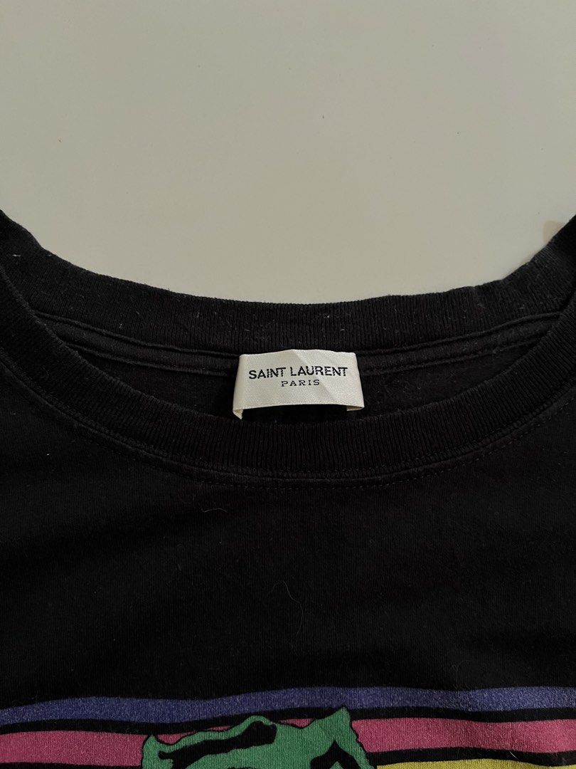Saint Laurent T-Rex Dinosaur Graphic Tee (Category: Tshirts & Polo Shirts ) located in Manila. Submitted by halukays (Listing ID 1471196182, Image 3). Description: - Brand: Saint Laurent - Color: Black - Material: 100% Cotton (Made in Italy) - Size: XS (Slim fit) - Design: Vibrant dinosaur graphic with retro stripes and star details on chest - Style: Crew neck, short sleeves, classic casual wear Size Medium Width 19 Length 27 Color rate 9/10 Good