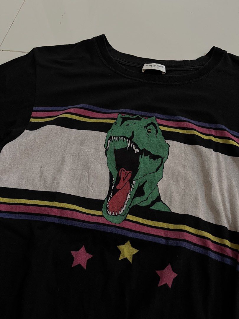 Saint Laurent T-Rex Dinosaur Graphic Tee (Category: Tshirts & Polo Shirts ) located in Manila. Submitted by halukays (Listing ID 1471196182, Image 2). Description: - Brand: Saint Laurent - Color: Black - Material: 100% Cotton (Made in Italy) - Size: XS (Slim fit) - Design: Vibrant dinosaur graphic with retro stripes and star details on chest - Style: Crew neck, short sleeves, classic casual wear Size Medium Width 19 Length 27 Color rate 9/10 Good