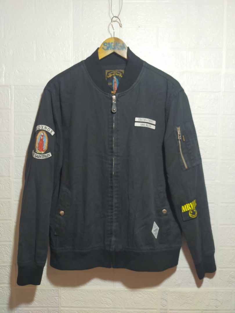 Saintpain Black Bomber Jacket with Patches (Category: Coats, Jackets and Outerwear) located in Valencia. Submitted by cabisaythriftshop (Listing ID 1471223551, Image 1). Description: - Brand: Saintpain - Color: Black - Material: Durable canvas - Closure: Full zip - Details: Ribbed collar, cuffs, and hem - Pockets: Utility pocket with zipper on the left sleeve - Patches: 'Faith & Trust God Bless' chest patch, Virgin Mary right sleeve graphic, and 