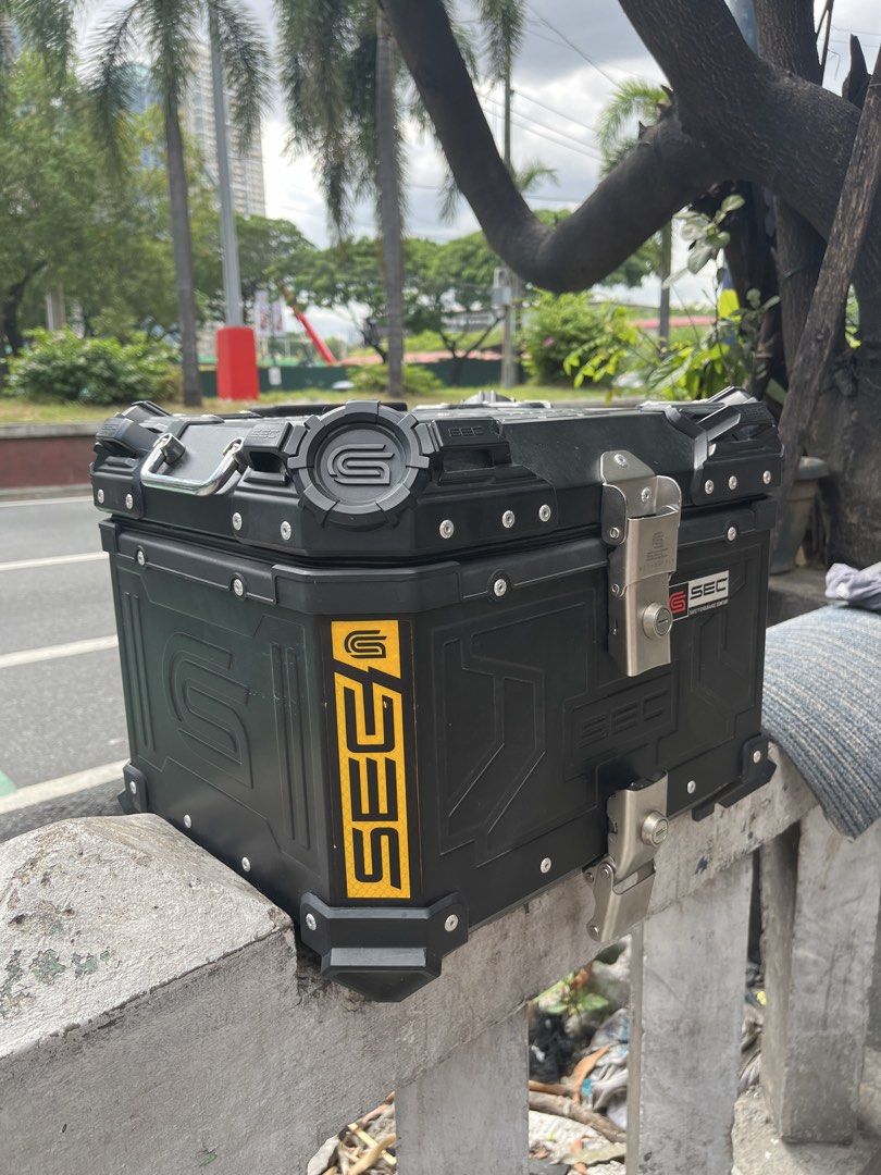 SEC Motorcycle Top Box Black Aluminum Storage (Category: Body Parts and Accessories) located in Manila. Submitted by yurimahboy (Listing ID 1471171945, Image 2). Description: - Brand: SEC Motorcycle Top Box - Color: Matte Black with reflective yellow side branding - Material: Sturdy, durable aluminum build - Security: Dual locking latches - Interior: Leatherette lining with SEC debossed pattern, lid organizer pockets, and cross straps - Extra: In