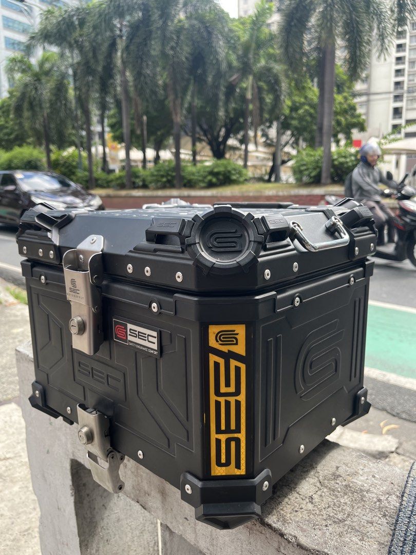 SEC Motorcycle Top Box Black Aluminum Storage (Category: Body Parts and Accessories) located in Manila. Submitted by yurimahboy (Listing ID 1471171945, Image 1). Description: - Brand: SEC Motorcycle Top Box - Color: Matte Black with reflective yellow side branding - Material: Sturdy, durable aluminum build - Security: Dual locking latches - Interior: Leatherette lining with SEC debossed pattern, lid organizer pockets, and cross straps - Extra: In