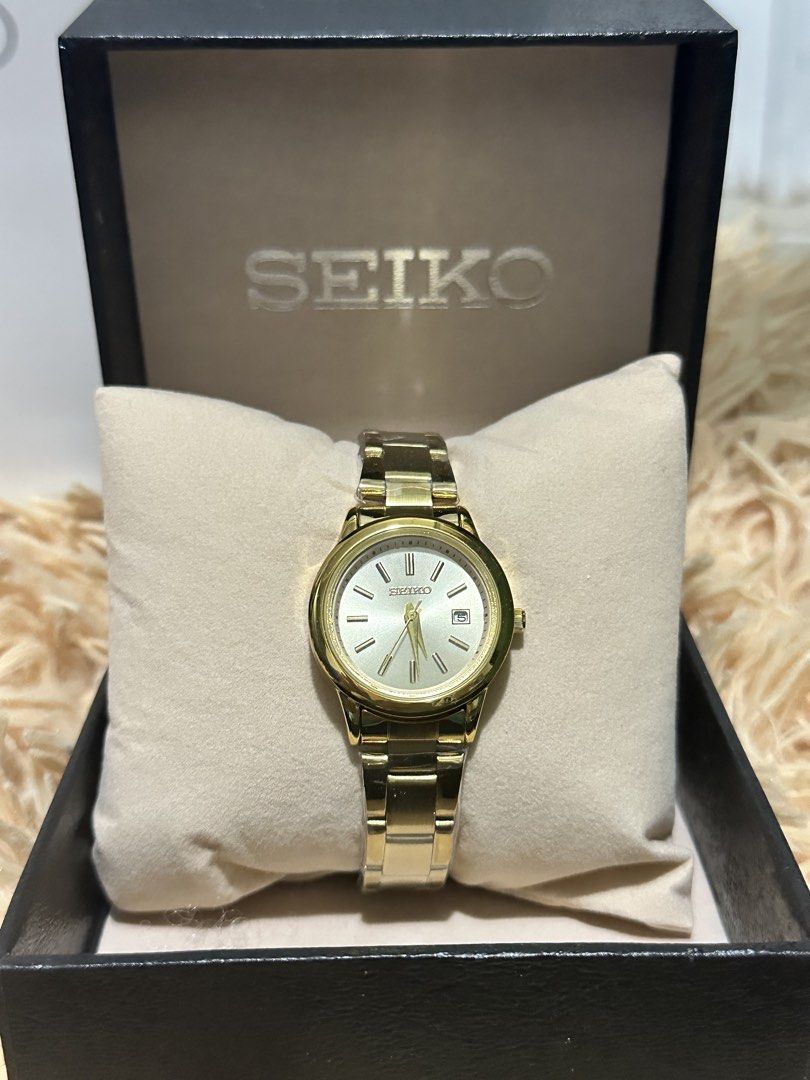 Seiko Gold Tone Watch with Box (Category: Women's Watches) located in Manila. Submitted by mbcollections251 (Listing ID 1471238000, Image 1). Description: Gold tone Seiko watch featuring a champagne dial, stick indices, and a date window at the 3 o'clock position. Matching gold metallic link bracelet with secure clasp closure. Includes original branded presentation box with fitted cream pillow. Classic dress piece suitable for daily wear or forma
