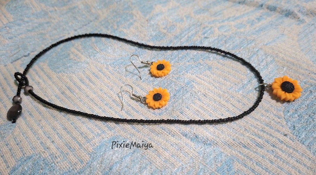 Sunflower Necklace and Earring Set (Category: Necklaces) located in Valenzuela. Submitted by pixieworks64309 (Listing ID 1471157328, Image 1). Description: - Matching sunflower jewelry set (necklace and earrings) - Features vibrant yellow and black sunflower charms - Necklace comes with a delicate black seed bead chain - Earrings designed with comfortable hook dangles - Perfect casual everyday accessories with a bright floral theme.
