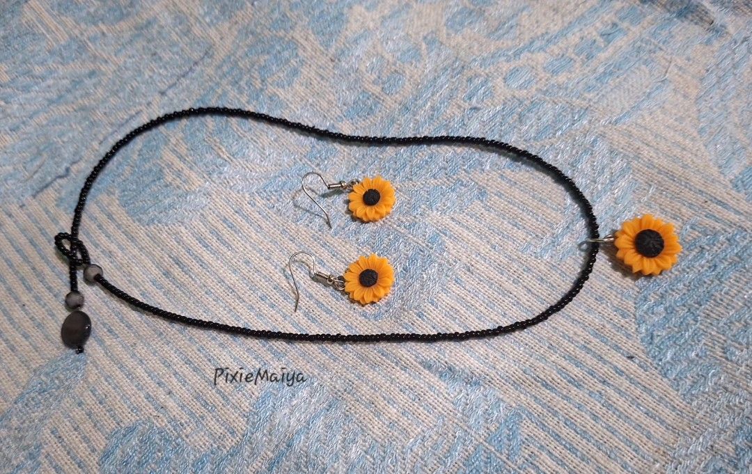 Sunflower Necklace and Earring Set (Category: Necklaces) located in Valenzuela. Submitted by pixieworks64309 (Listing ID 1471157328, Image 2). Description: - Matching sunflower jewelry set (necklace and earrings) - Features vibrant yellow and black sunflower charms - Necklace comes with a delicate black seed bead chain - Earrings designed with comfortable hook dangles - Perfect casual everyday accessories with a bright floral theme.
