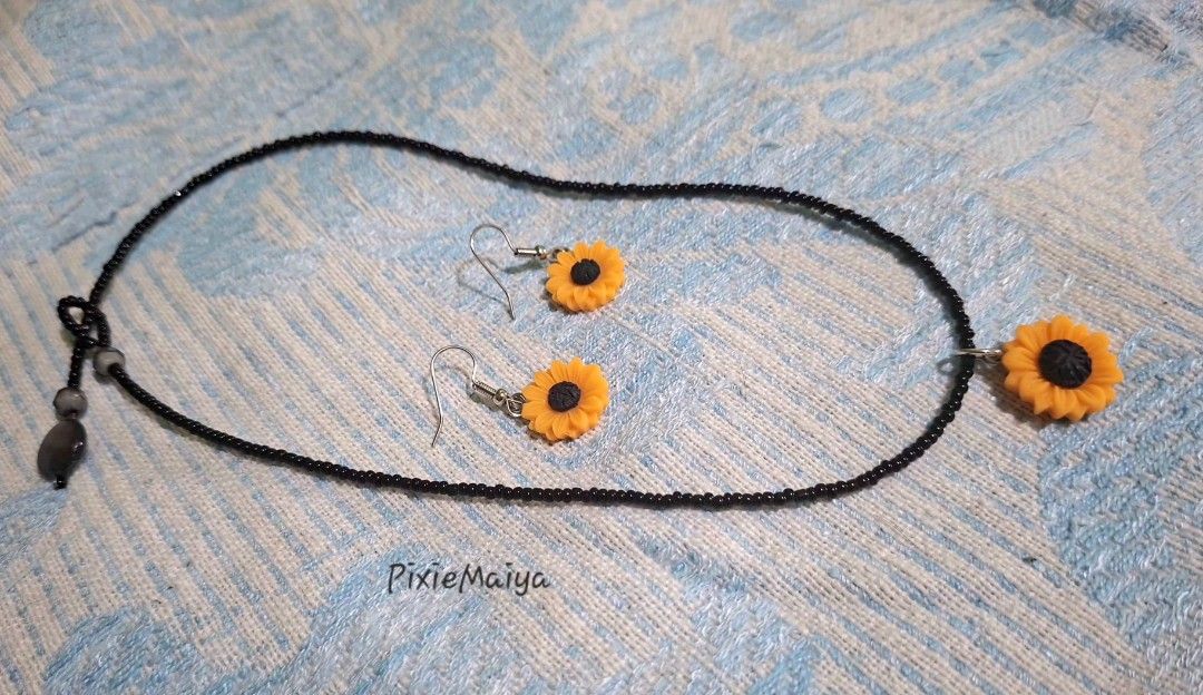 Sunflower Necklace and Earring Set (Category: Necklaces) located in Valenzuela. Submitted by pixieworks64309 (Listing ID 1471157328, Image 3). Description: - Matching sunflower jewelry set (necklace and earrings) - Features vibrant yellow and black sunflower charms - Necklace comes with a delicate black seed bead chain - Earrings designed with comfortable hook dangles - Perfect casual everyday accessories with a bright floral theme.