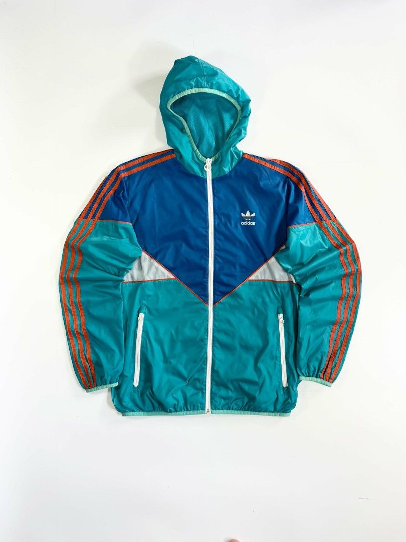 Vintage Adidas Windbreaker (Category: Coats, Jackets and Outerwear) located in Valenzuela. Submitted by veriez_gems (Listing ID 1471269128, Image 1). Description: Adidas Originals (featuring classic Trefoil logo branding) ​Colorway: Dynamic multi-color blocking featuring teal green, deep royal blue, crisp white chevron accents, and vivid orange 3-stripes ​Design & Fit Features: ​Full-zip front closure with a fitted hood for stylish coverage ​Clas
