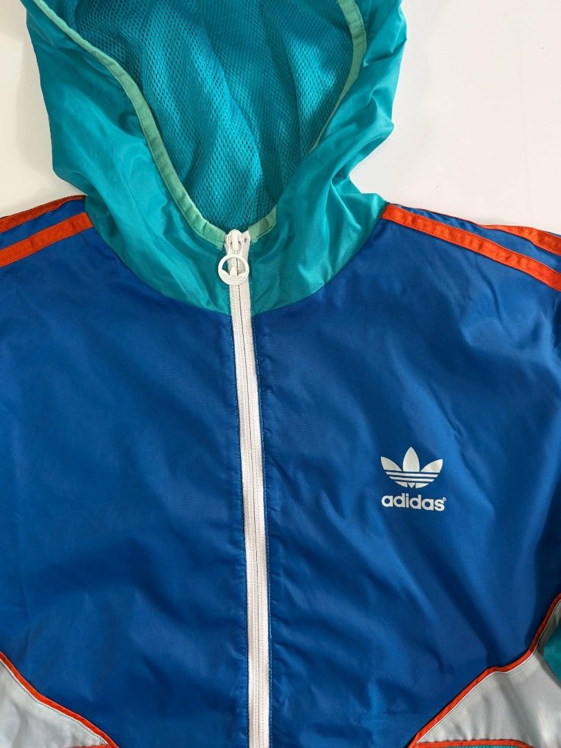 Vintage Adidas Windbreaker (Category: Coats, Jackets and Outerwear) located in Valenzuela. Submitted by veriez_gems (Listing ID 1471269128, Image 2). Description: Adidas Originals (featuring classic Trefoil logo branding) ​Colorway: Dynamic multi-color blocking featuring teal green, deep royal blue, crisp white chevron accents, and vivid orange 3-stripes ​Design & Fit Features: ​Full-zip front closure with a fitted hood for stylish coverage ​Clas