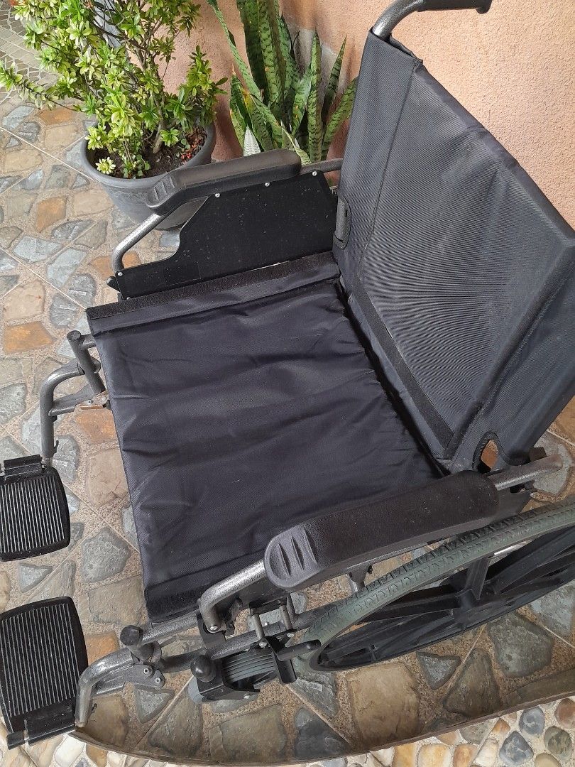 Wheelchair Heavy Duty (Category: Wheelchairs) located in Silang. Submitted by trish125 (Listing ID 1471197888, Image 3). Description: - Condition: Clean and 100% working smoothly - Frame: Sturdy grey metal with black fabric seat - Mobility: Large rear wheels with hand rims and small front casters - Features: Includes footrests - Portability: Folds up easily for car trunk storage - Fulfillment: Ready for pickup.