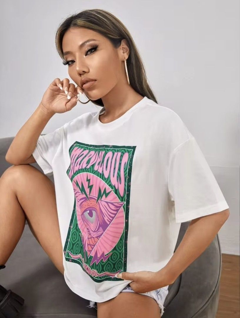White T-Shirt with Marvelous Graphic Print (Category: Shirts) located in Manila. Submitted by babeboxtheory (Listing ID 1471171756, Image 2). Description: - Style: Casual short-sleeve t-shirt with a relaxed fit and classic crew neck - Design: Eye-catching 'MARVELOUS' front print in pink over a psychedelic eye and lightning bolt graphic - Color: Crisp white base with a vibrant green patterned background.