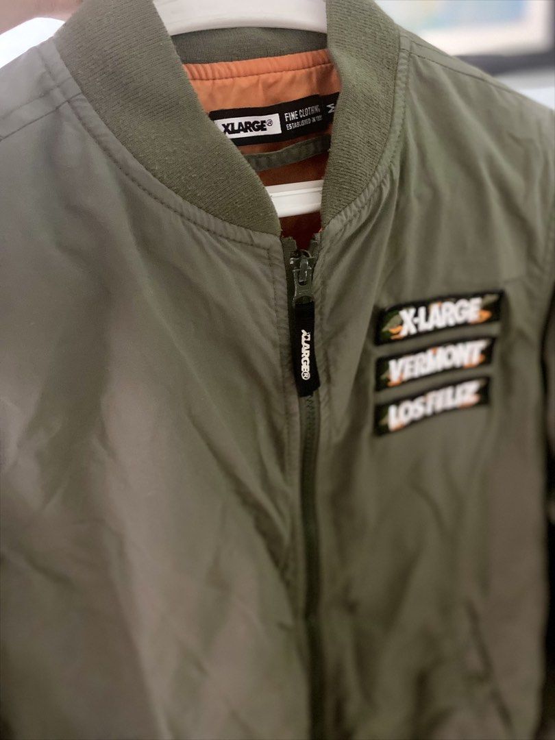 XLARGE Green Bomber Jacket with Patches Size M (Category: Coats, Jackets and Outerwear) located in Manila. Submitted by japanstreetwear (Listing ID 1471223957, Image 2). Description: - Brand: XLARGE - Style: Classic streetwear bomber jacket - Color: Olive green with bright orange lining - Size: Medium - Details: Embroidered chest patches (X-LARGE, VERMONT, LOS FELIZ), large white text logo on the back, branded zip pull tab - Pockets: Two front ha