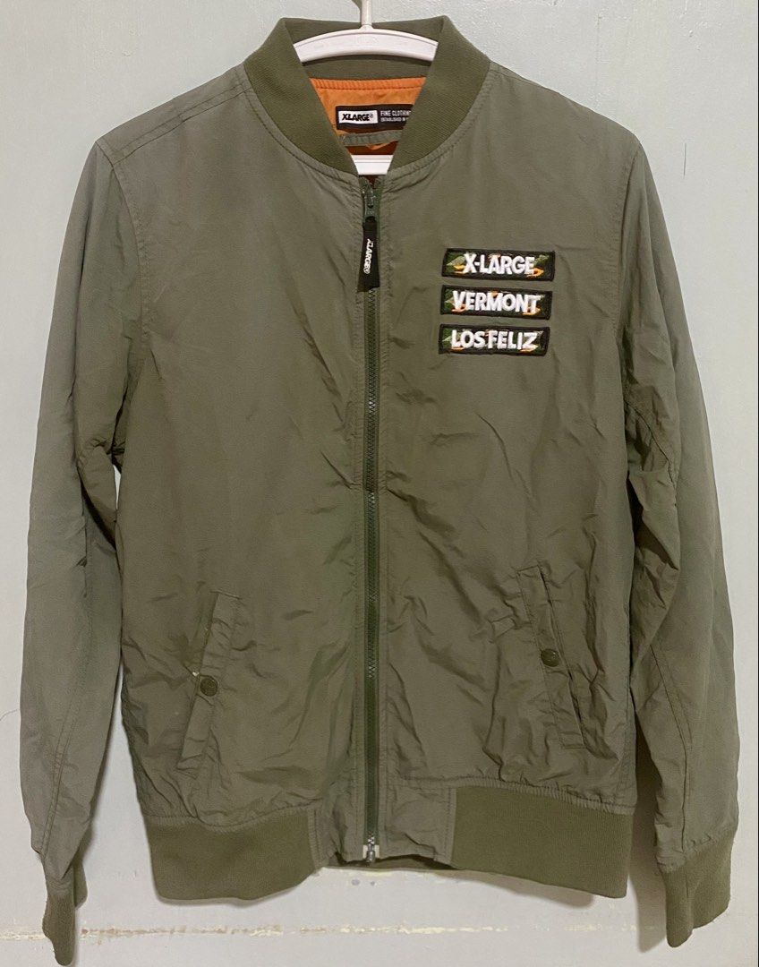 XLARGE Green Bomber Jacket with Patches Size M (Category: Coats, Jackets and Outerwear) located in Manila. Submitted by japanstreetwear (Listing ID 1471223957, Image 1). Description: - Brand: XLARGE - Style: Classic streetwear bomber jacket - Color: Olive green with bright orange lining - Size: Medium - Details: Embroidered chest patches (X-LARGE, VERMONT, LOS FELIZ), large white text logo on the back, branded zip pull tab - Pockets: Two front ha