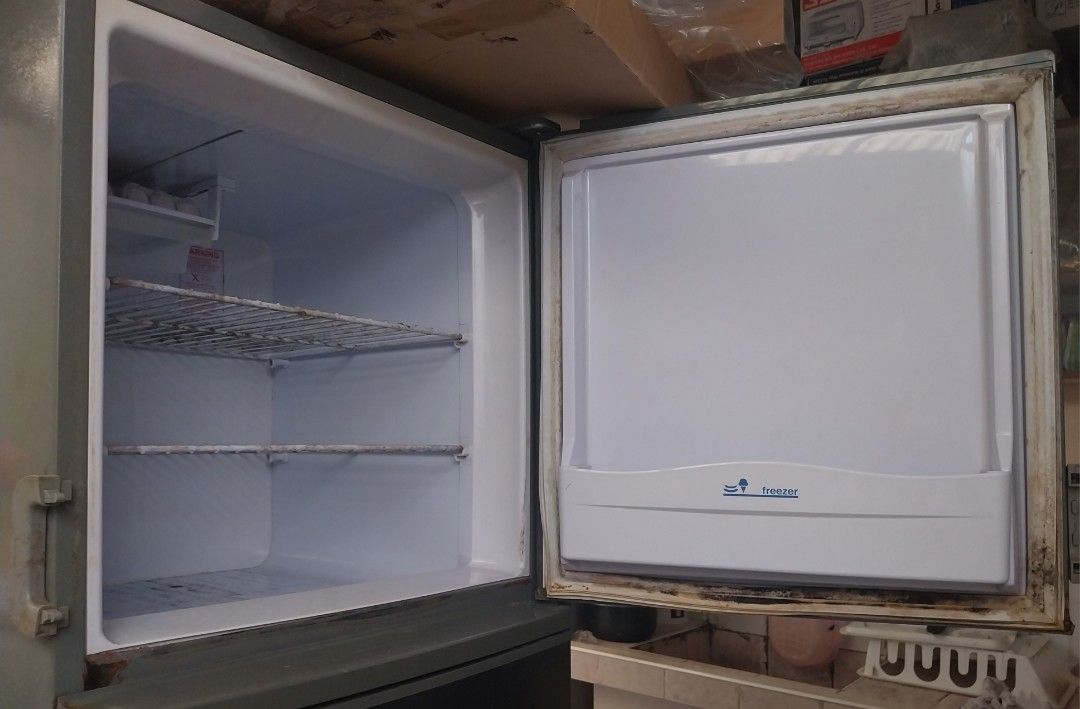 Condura Two-Door Refrigerator (Category: Refrigerators and Freezers) located in Pasig City. Submitted by rare.ashima25 (Listing ID 1471338085, Image 2). Description: Condura two-door fridge in dark gray finish. Top freezer compartment includes wire shelving and door pocket. Main lower section has standard shelving space. Exterior shows smudges and wear marks. Rubber seals around doors show visible dirt accumulation and staining. Clean-up needed b
