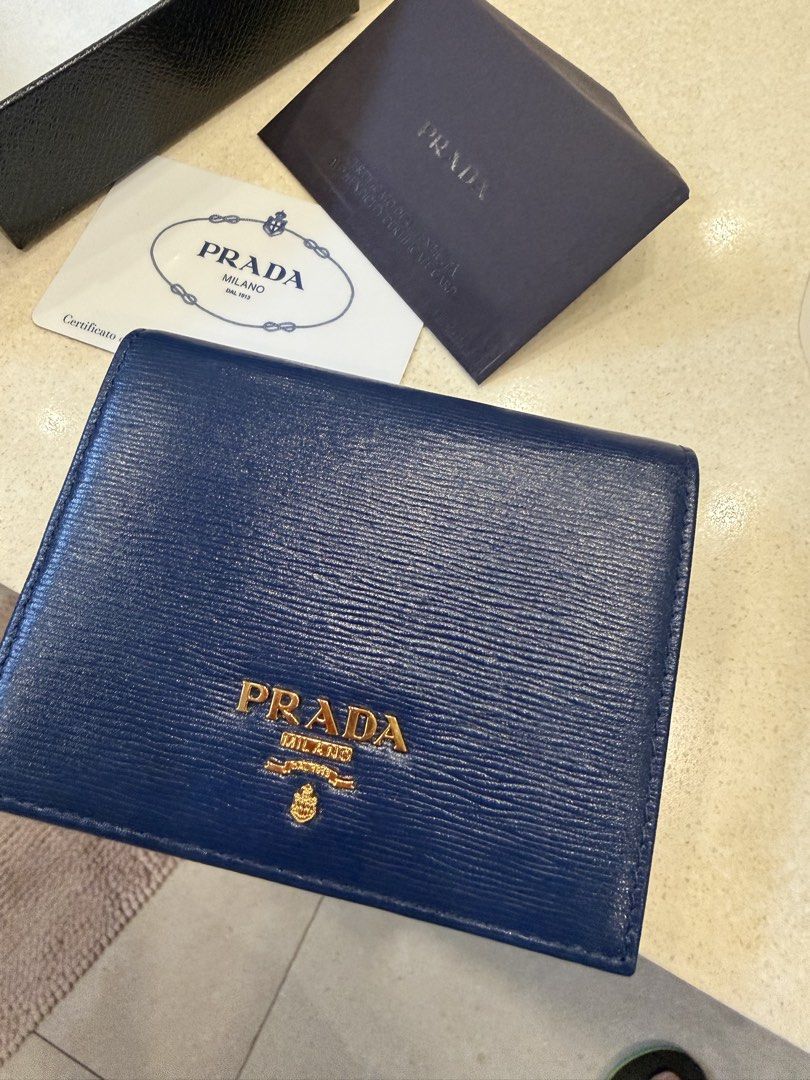 Prada Blue Saffiano Leather Compact Wallet with Box (Category: Luxury Bags & Wallets) located in Mandaluyong City. Submitted by jenut (Listing ID 1471297841, Image 2). Description: - Brand: Prada - Material: Saffiano leather - Color: Deep Blue with gold-tone hardware - Features: Card slots, bill compartment, and snap coin pocket - Condition: Excellent (clean inside and out) - Inclusions: Original Prada box and authenticity certificate card - Mode