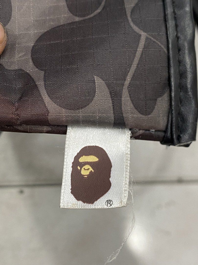 A Bathing Ape Bape Camo Tote Bag (Category: Tote Bags) located in General Trias. Submitted by mangu_ukay (Listing ID 1465952952, Image 3). Description: - Authentic BAPE black camouflage tote bag - Durable grid pattern ripstop material with black faux leather handles and trim - Roomy open-top main compartment with clean fabric lining - Signature small BAPE ape head logo tag on the side seam - Versatile and spacious everyday carryall - Condition: B