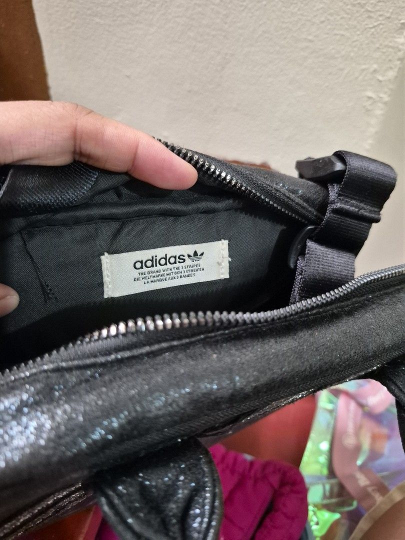 Adidas Black Glitter Mini Handbag (Category: Luxury Bags & Wallets) located in Antipolo. Submitted by prinsesa_dianne (Listing ID 1465940362, Image 2). Description: - Brand: Adidas - Style: Mini handbag / everyday casual bag - Color/Design: Black glitter with silver three stripes on the front - Closure & Handles: Secure zipper closure with dual carry handles - Interior: Clean fabric lining featuring the classic Adidas brand logo label patch - Con