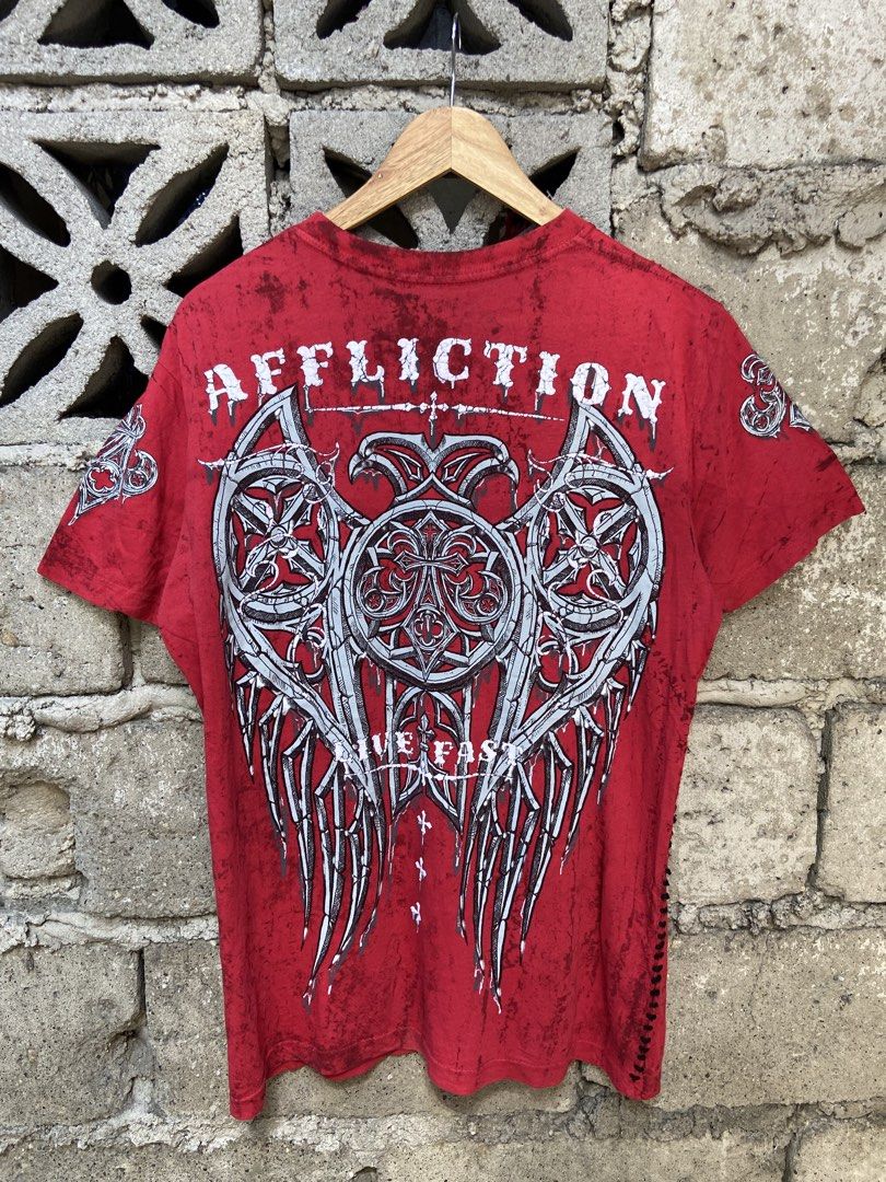 Affliction Live Fast Red Graphic Tee (Category: Tshirts & Polo Shirts ) located in Binan City. Submitted by doze16 (Listing ID 1465929486, Image 2). Description: - Brand/Style: Red Affliction graphic t-shirt - Design: Large front and back prints with ornate cross and wing details - Finish: Distressed wash with unique side accent stitching - Size: 21 inches pit to pit, 27 inches length - Aesthetic: Heavy metal and Y2K streetwear vibe.
