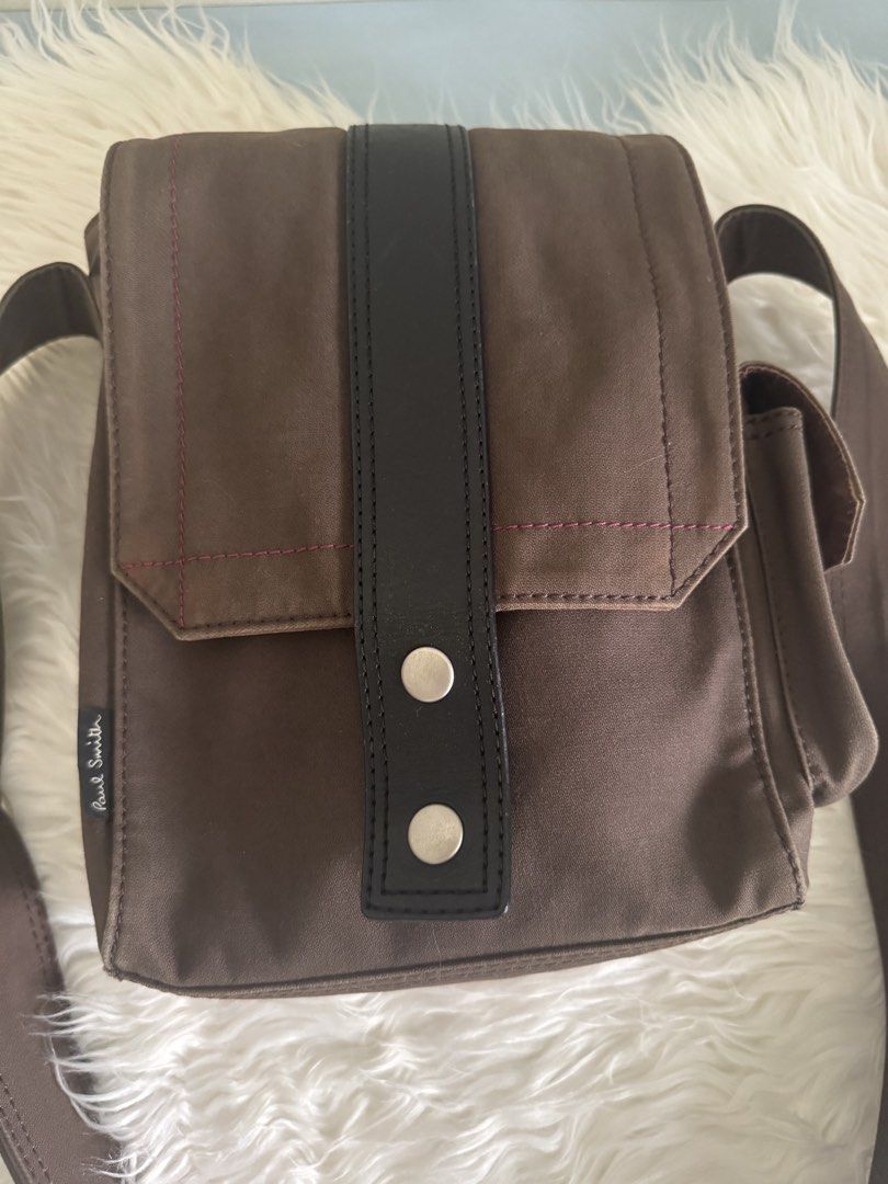 Authentic Paul Smith Brown Canvas Crossbody Bag with Adjustsble Strap (Category: Sling Bags) located in Pasig City. Submitted by topbrandpursuits (Listing ID 1465804920, Image 3). Description: - Authentic Paul Smith crossbody bag in durable brown canvas - Features a striking vertical black leather center stripe - Eye-catching contrast pink stitching on the front flap and side pocket - Convenient side pocket with velcro closure - Adjustable brown 