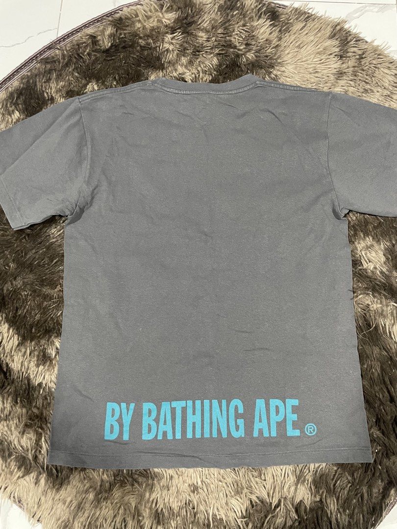 BAPE A Bathing Ape Big Head (Category: Tshirts & Polo Shirts ) located in Calapan. Submitted by lucasthrifts (Listing ID 1465921547, Image 2). Description: - Brand: A Bathing Ape (BAPE) - Color: Grey - Size: S (Width: 18", Length: 24”) - Design: Large blue ape head graphic on front, 'BY BATHING APE' lettering on lower back - Details: Classic crew neck, short sleeves, woven ape tag on left sleeve - Condition: Presentable - 100% authentic and ready